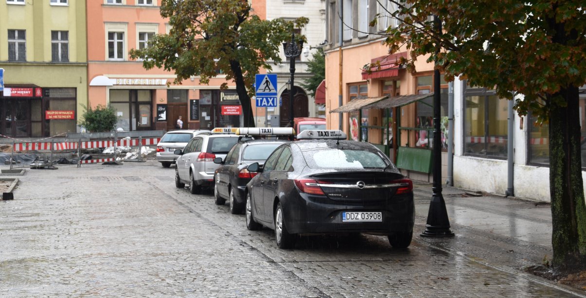 Trzy taksówki stojące na postoju w rynku, obok kamienice