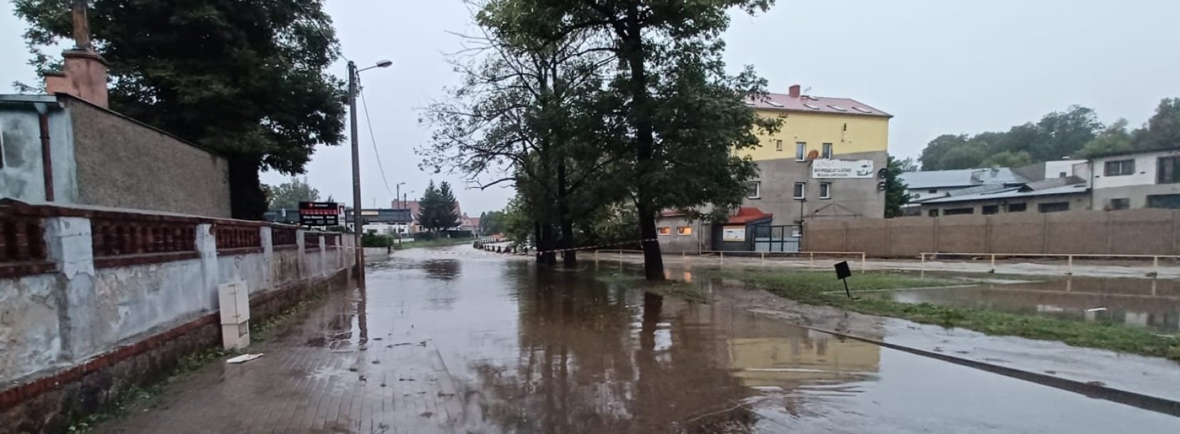 Droga zalana wodą, obok koryto rzeki pełne wody