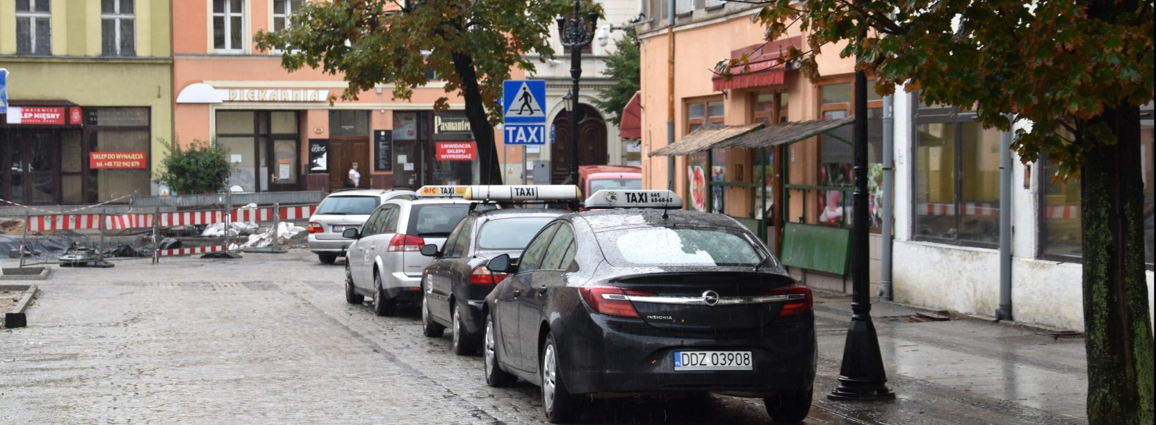 Trzy taksówki stojące na postoju w rynku, obok kamienice