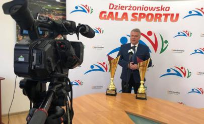 Burmistrz Dzierżoniowa na ściance promocyjnej ze sportowymi pucharami