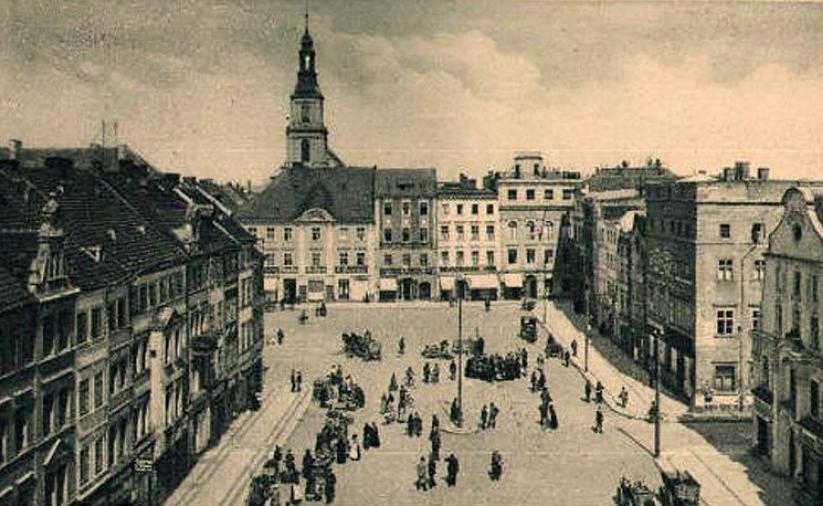 Rynek ze spacerującymi mieszkańcami i końmi ciągnącymi wozy