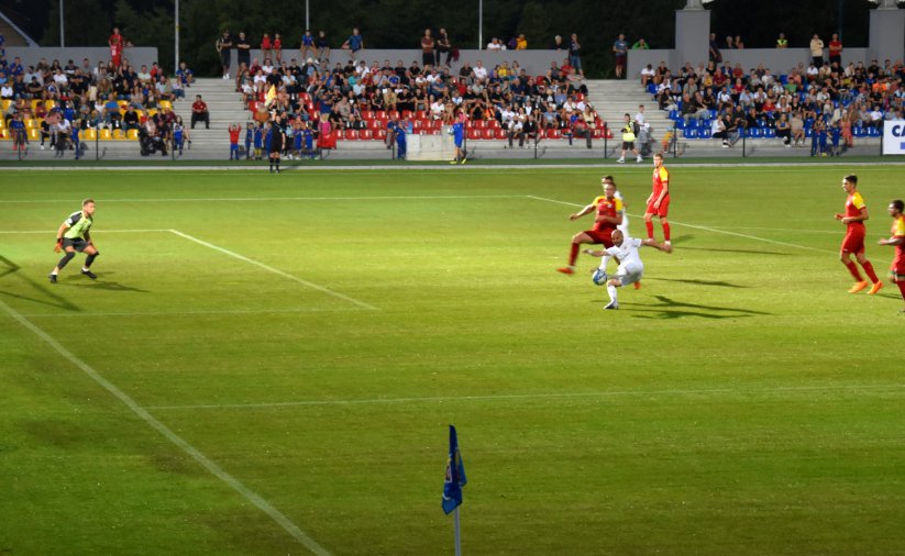 Piłkarze grający mecz na stadionie, w drugim planie trybuny z kibicami