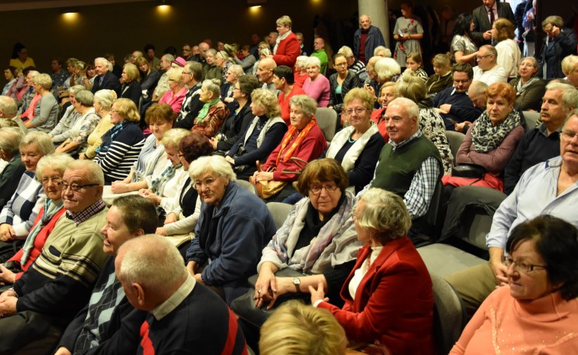 Kilkudziesięciu seniorów siedzących na krzesałach w sali ośrodka kultury