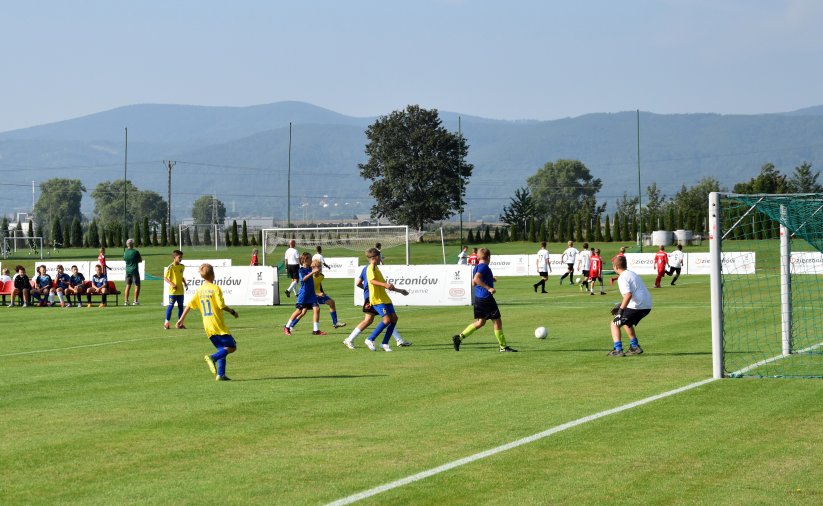 Mecz piłki nożnej, trawiaste boisko. zawodnicy w żółtych i błękitnych strojach, w tle panorama gór