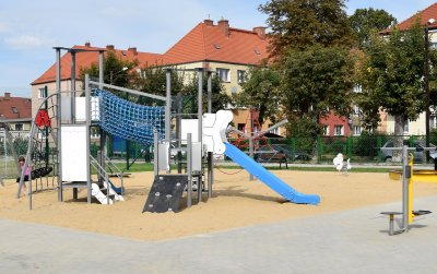 Nowy plac zabaw, piaszczyste podłoże, urządzenia do zabawy, w tle drzewa i budynki mieszkalne