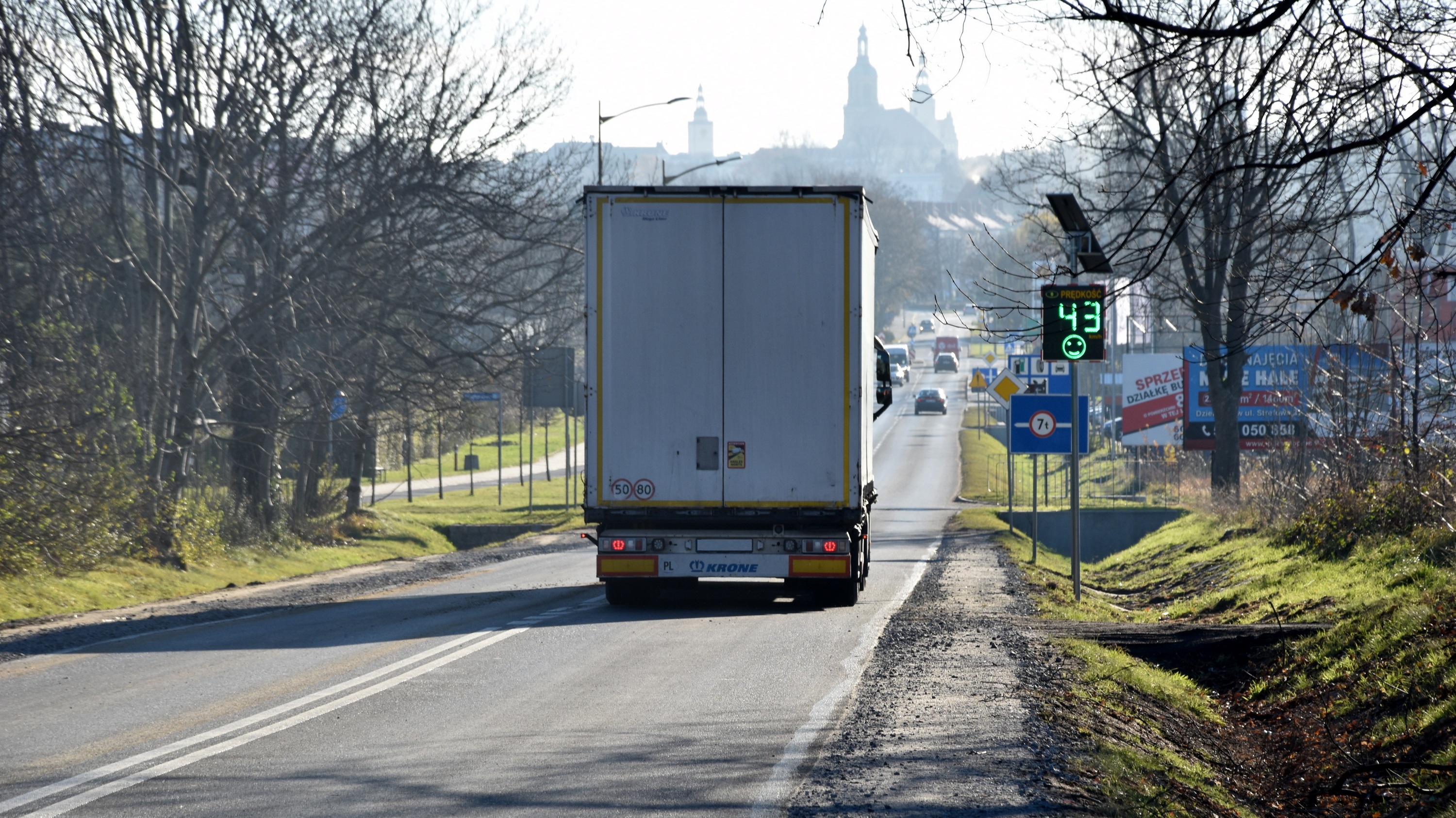 Ciężarówka jadąca drogą wjazdową do Dzierżoniowa, na poboczu tablica informująca kierowców o prędkości