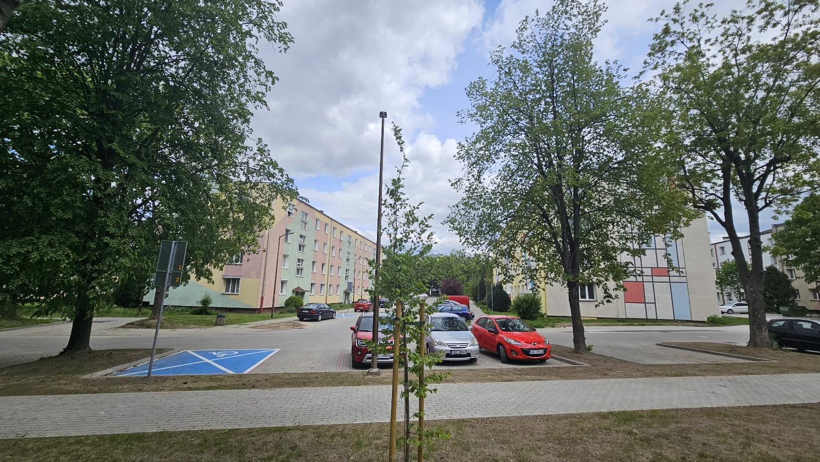 Fragment osiedla, na piewszym planie chodnik i droga z kostki betonowej, w tle budynki