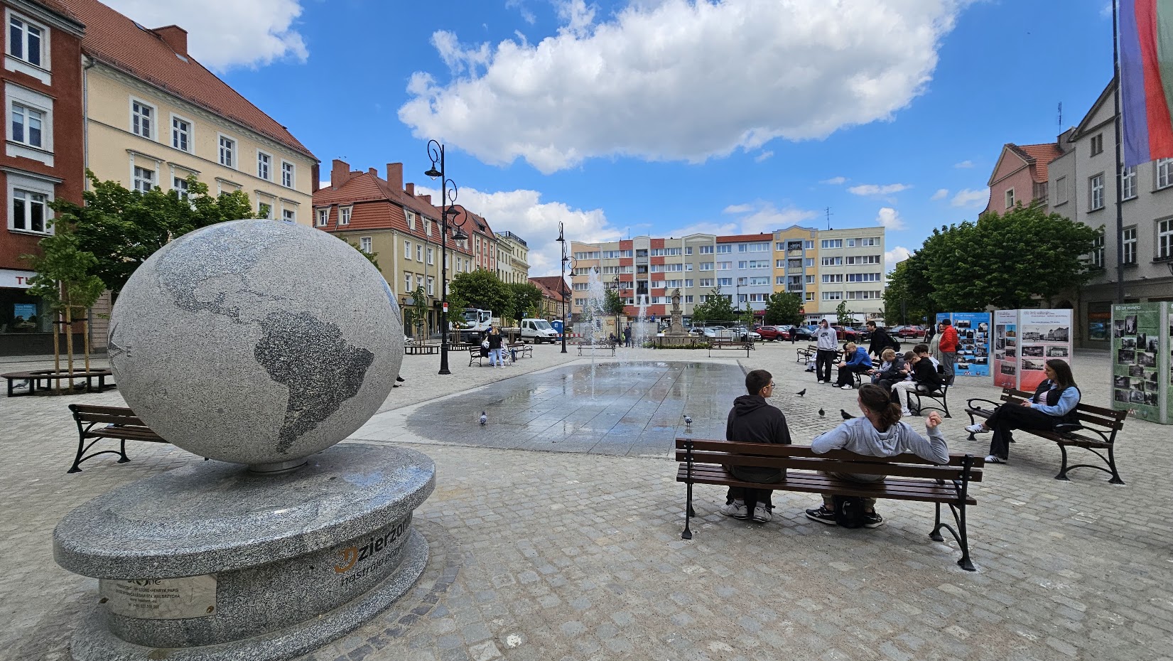 Rynek, ludzie siedzący na ławkach, pl lewej ogromny kamienny globus