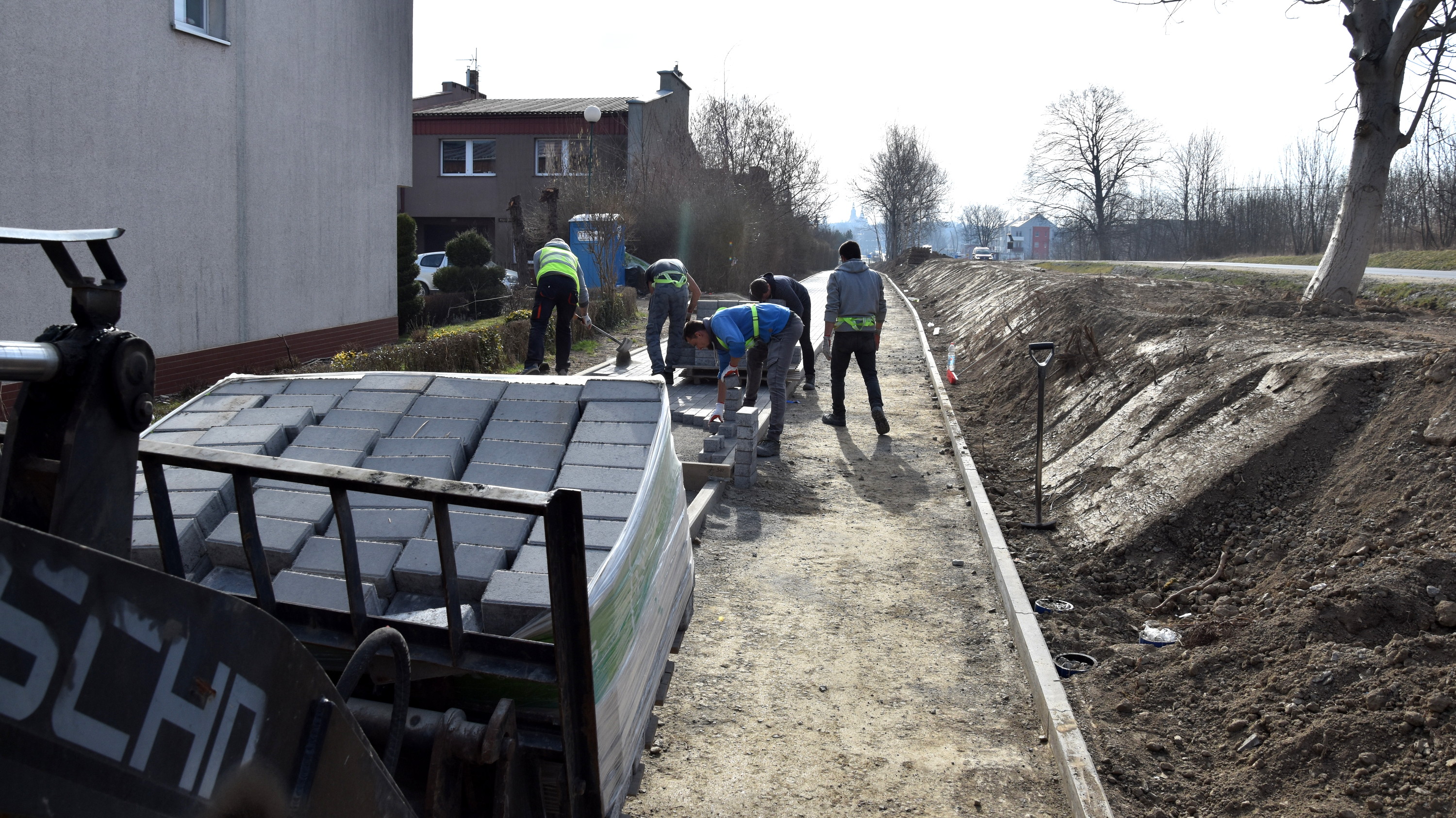 Pięciu mężczyzn pracujących przy ukłądaniu chodnika z kostki betonowej