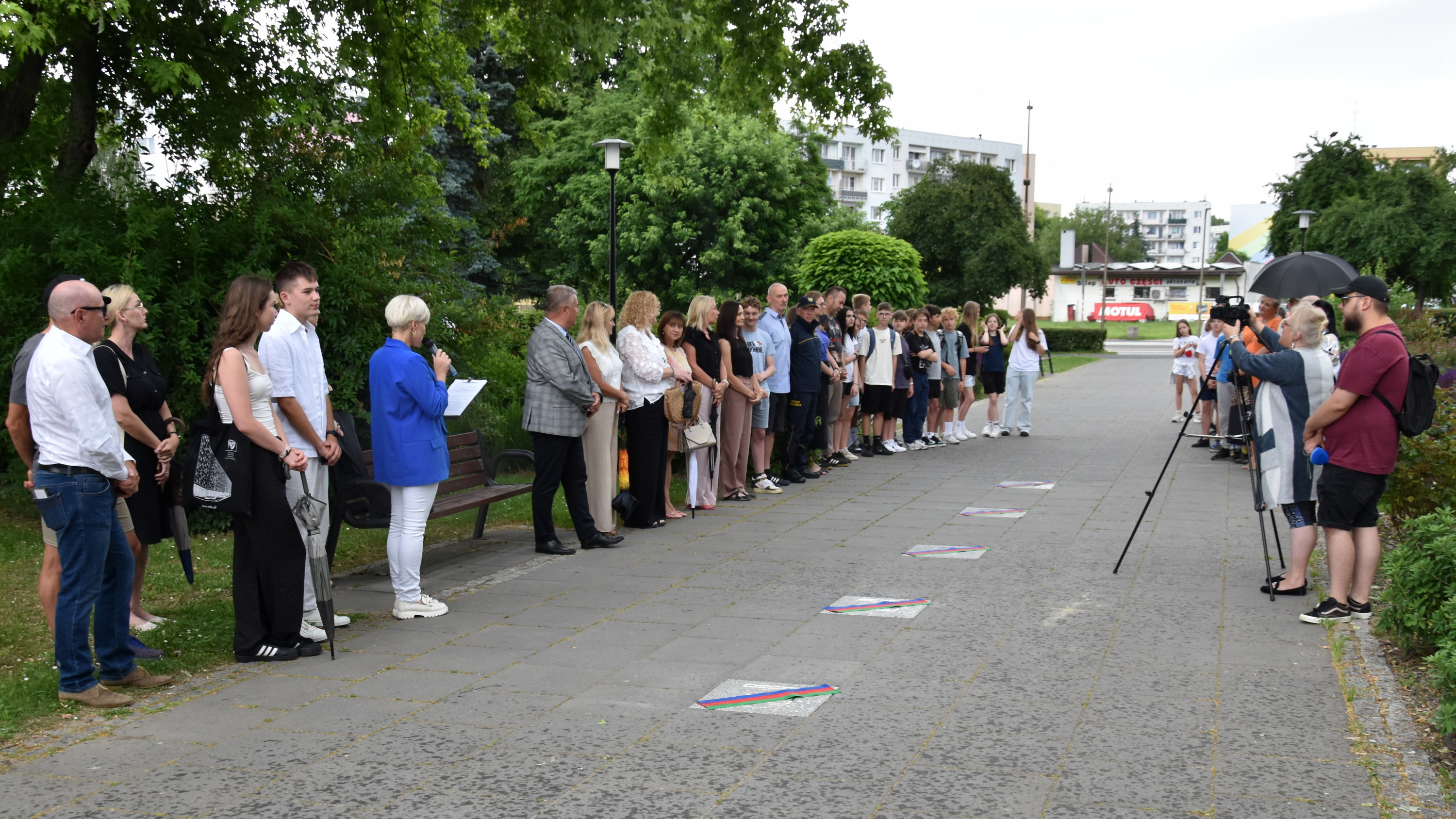 Aleja w parku miejskim, po bokach dwie gupy ludzi