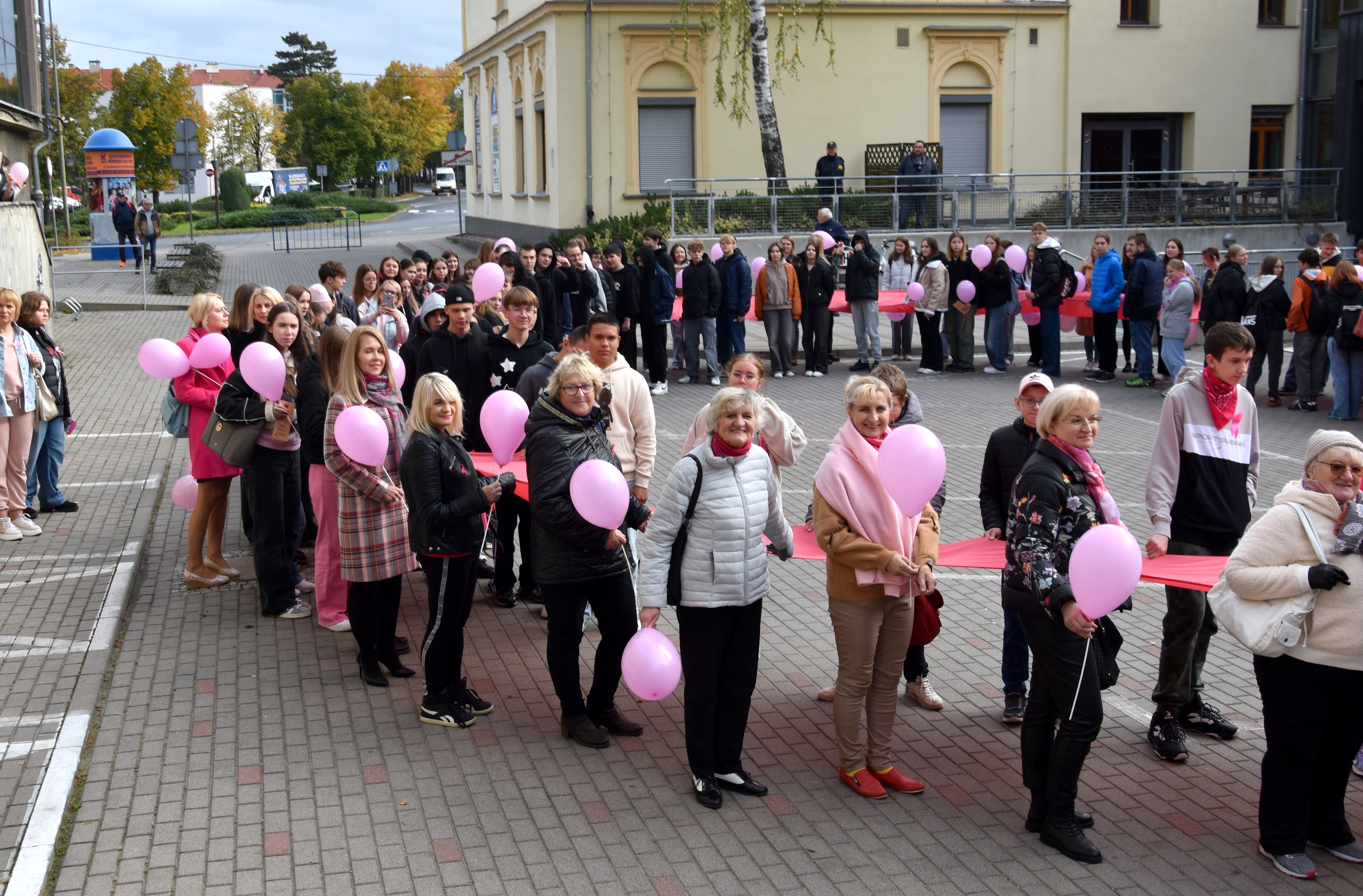 Mieszkańcy w różnym wieku trzymający wspólnie różową wstążkę i różowe balony