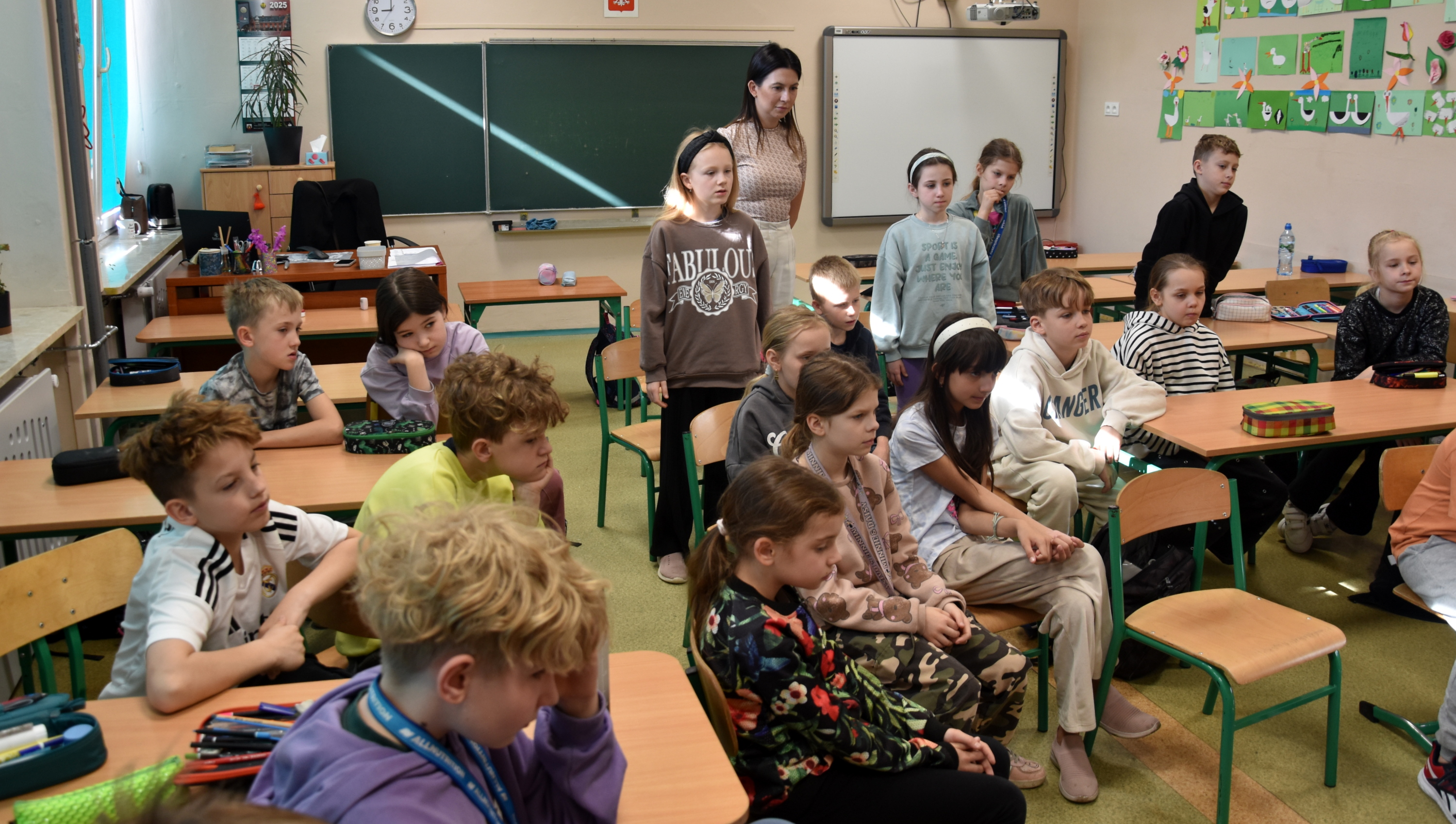 Ucnziowie wławkach szkolnych patrzący na prezentację udzielania pierwszej pomocy