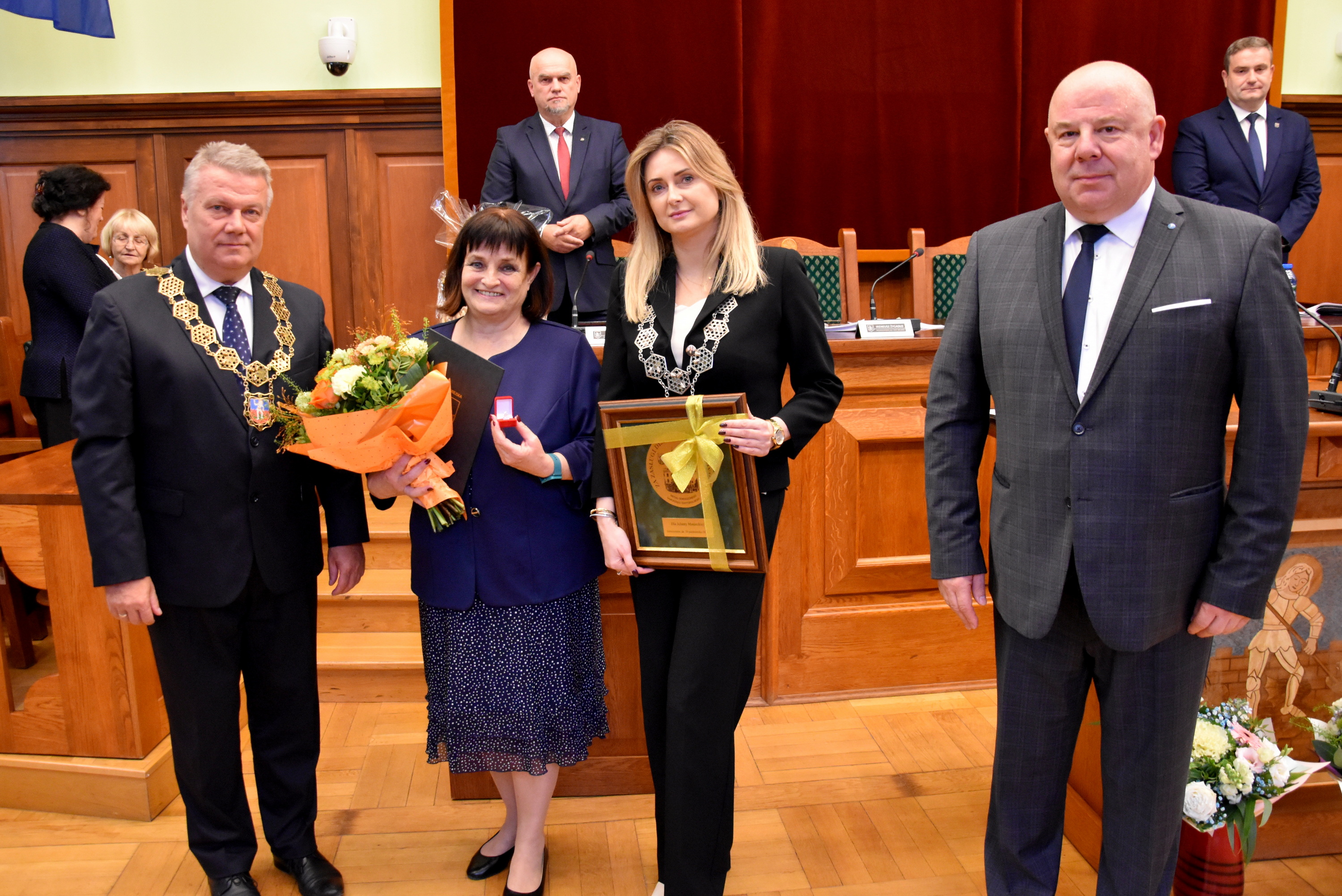 Jolanta Maniecka odbiera tytuł zasłużónego podczas sesji, obok niej burmistrz i przewodniczący rady 