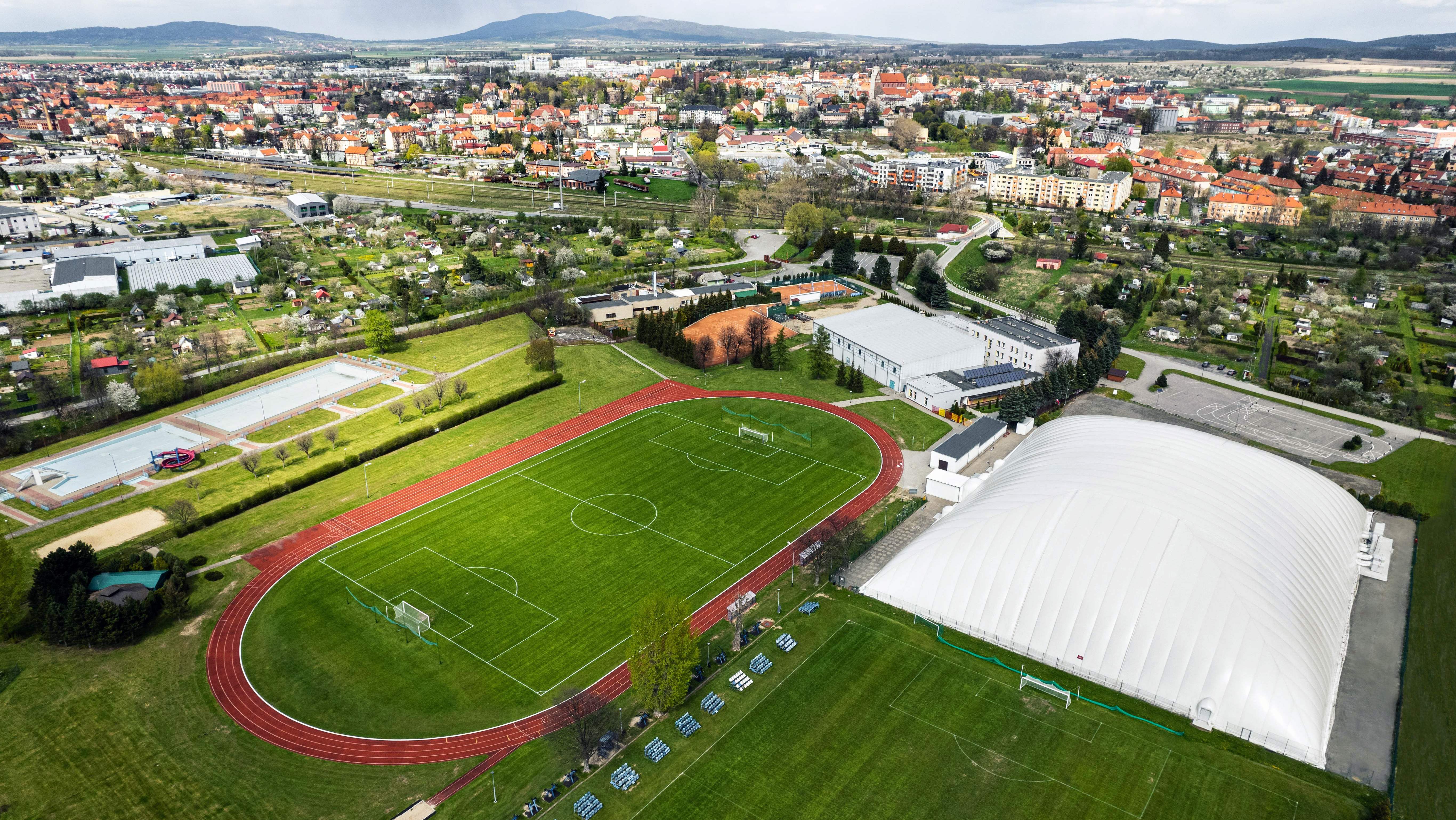 Ośrodek sportu z góry, widoczne boiska, dwie hale sportowe korty, basen i bieżnia