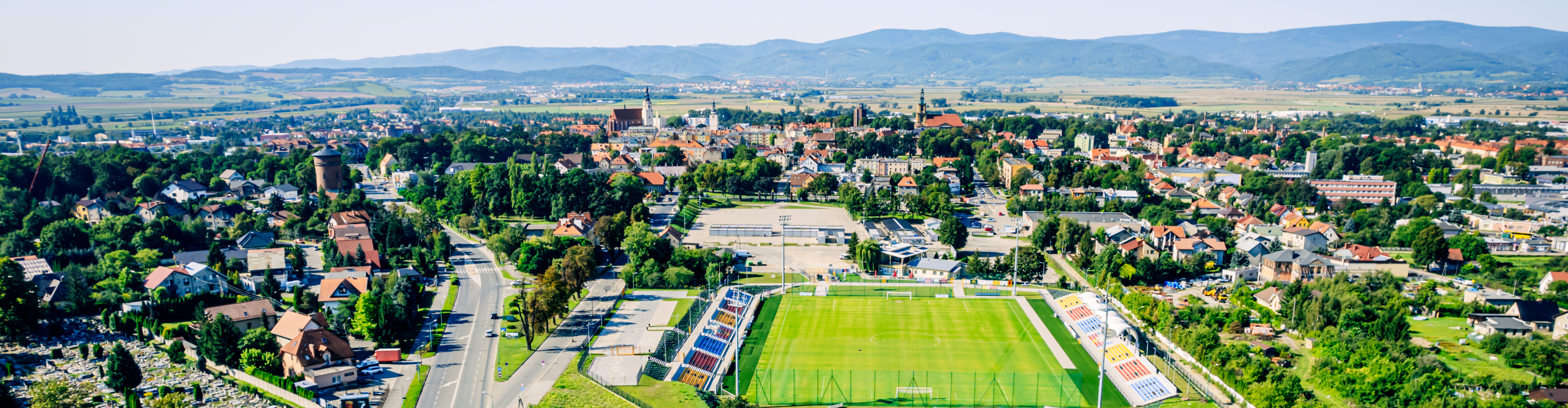 Dzierżoniów z lotu ptaka, na pierwszym planie stadion i panorama miasta, w tle góry