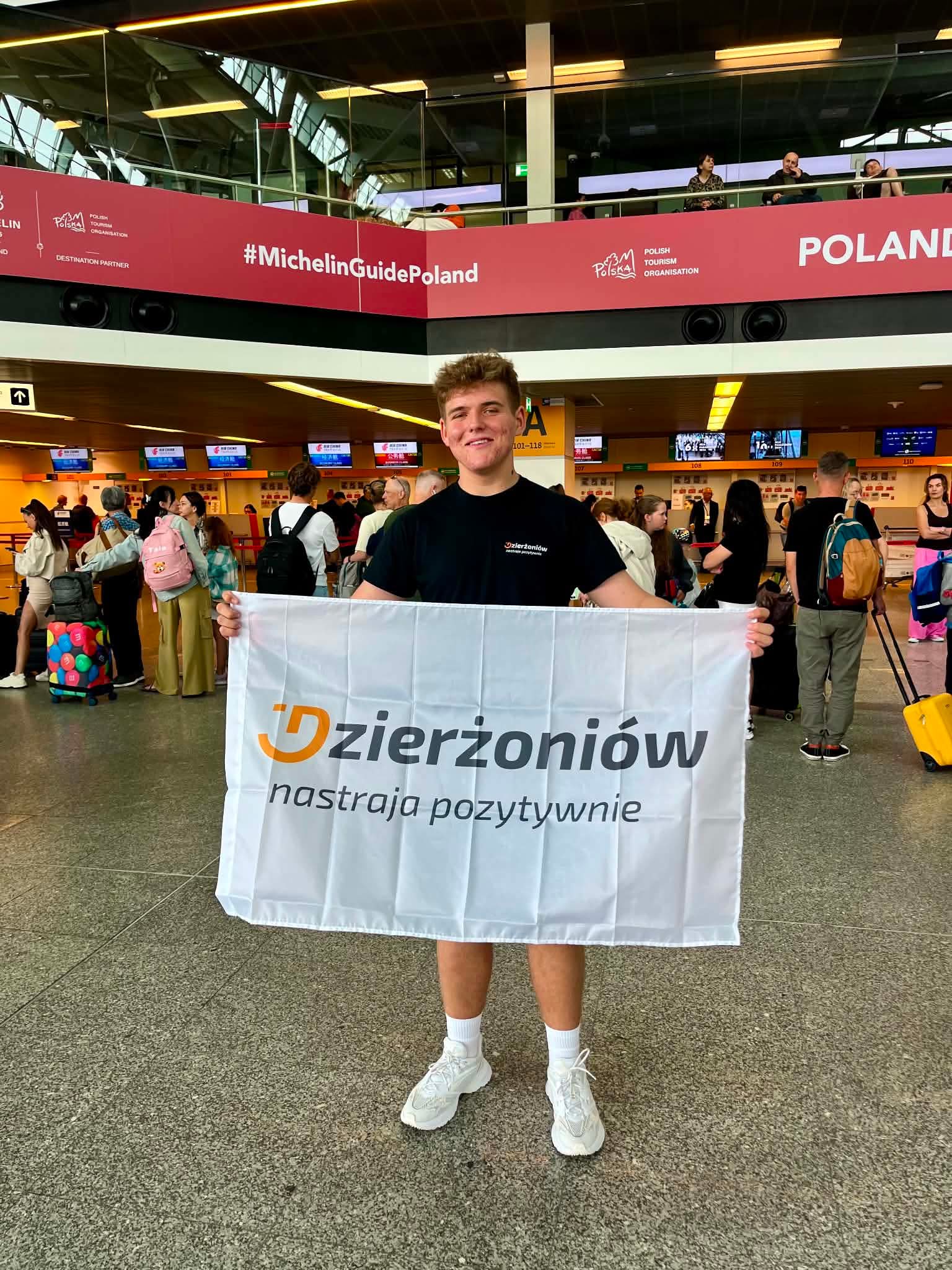 Marcel Mazurkiwicz na lotnisku w Chinach z flagą Dzierżoniów Nastraja Pozytywnie