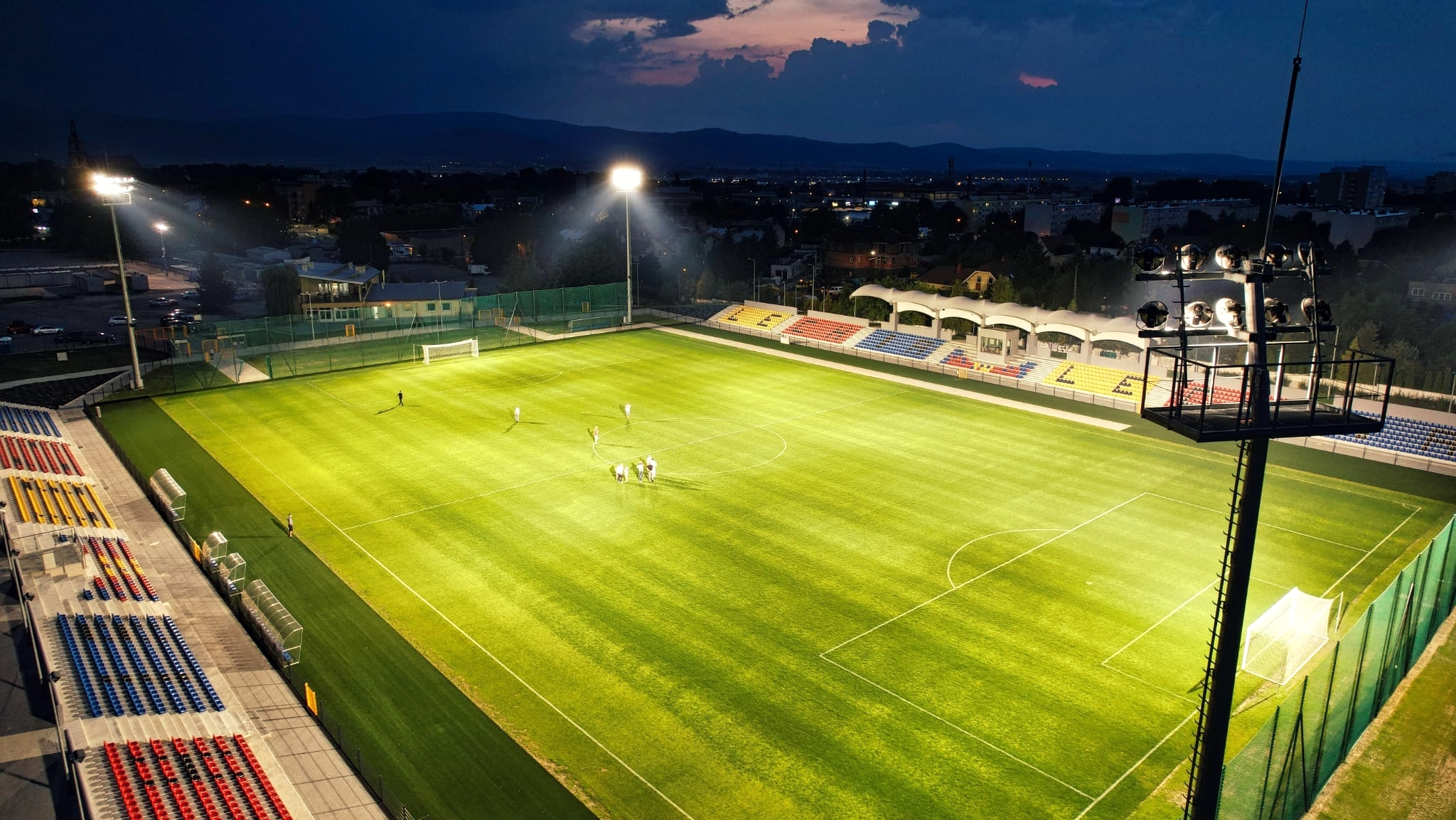 Stadion w Dzierżoniowie z góry. Noc, podświetlona murawa i trybuny, grupka piłkarzy na środku murawy 