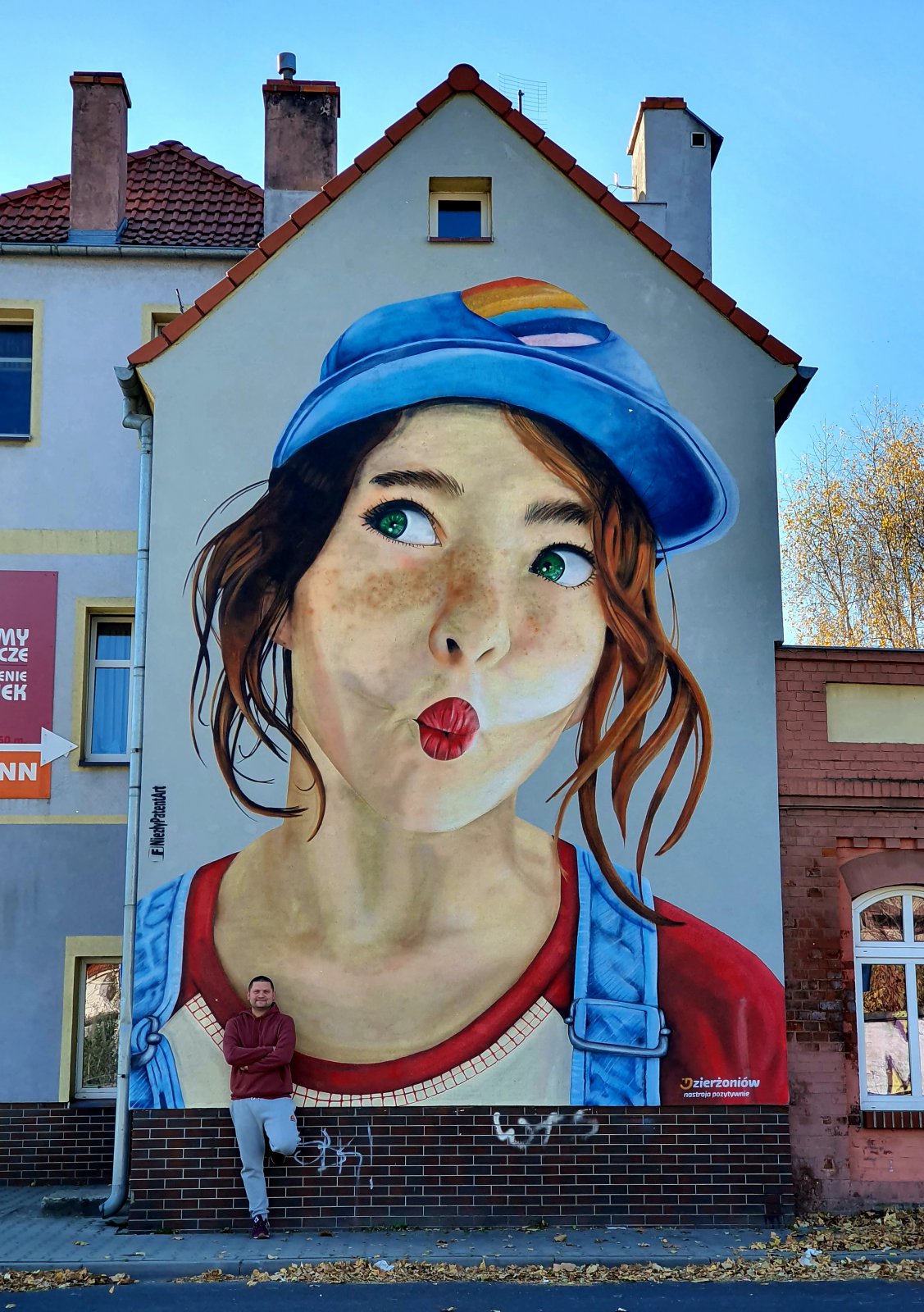 Mural, twarz młodej dziewczyny, przy muralu stroi jego autor