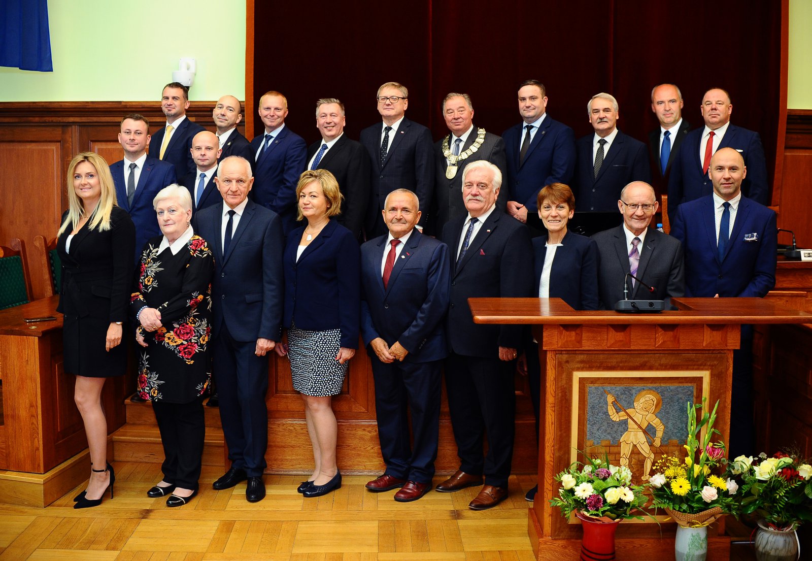 Grupowe zdjęcie 21 radnych w sali, w któej odbywaja sie obrady