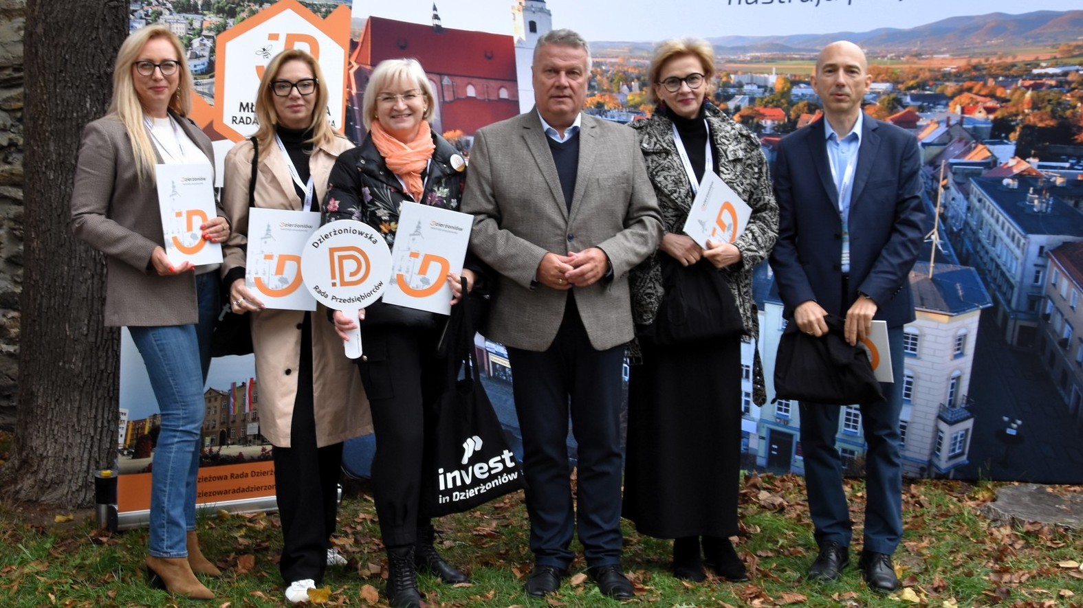 Pięcioro członków rady przedsiębiorców i burmistrz na tle ścianki ze zdjęciem miasta z góry