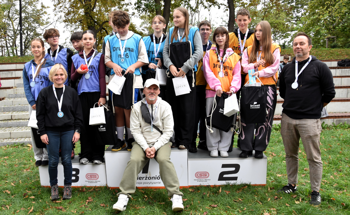 Kilkunastu uczestników gry terenowej na podium ustawionym w parku