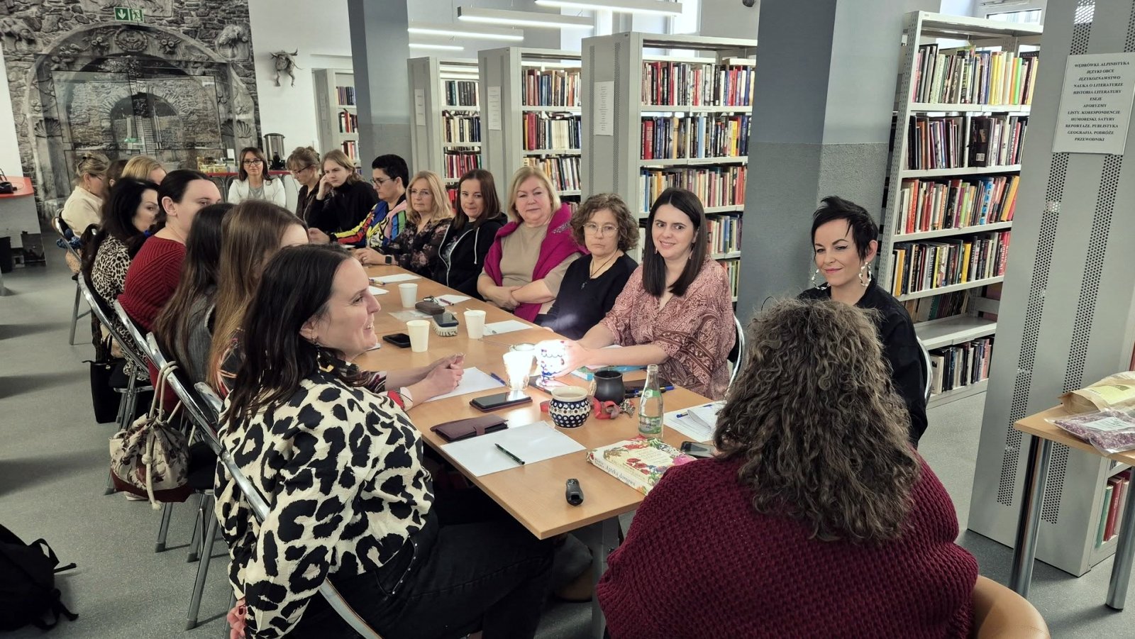 Kilkanaście kobiet siedzących przy długim stole, po bokach regały z książkami