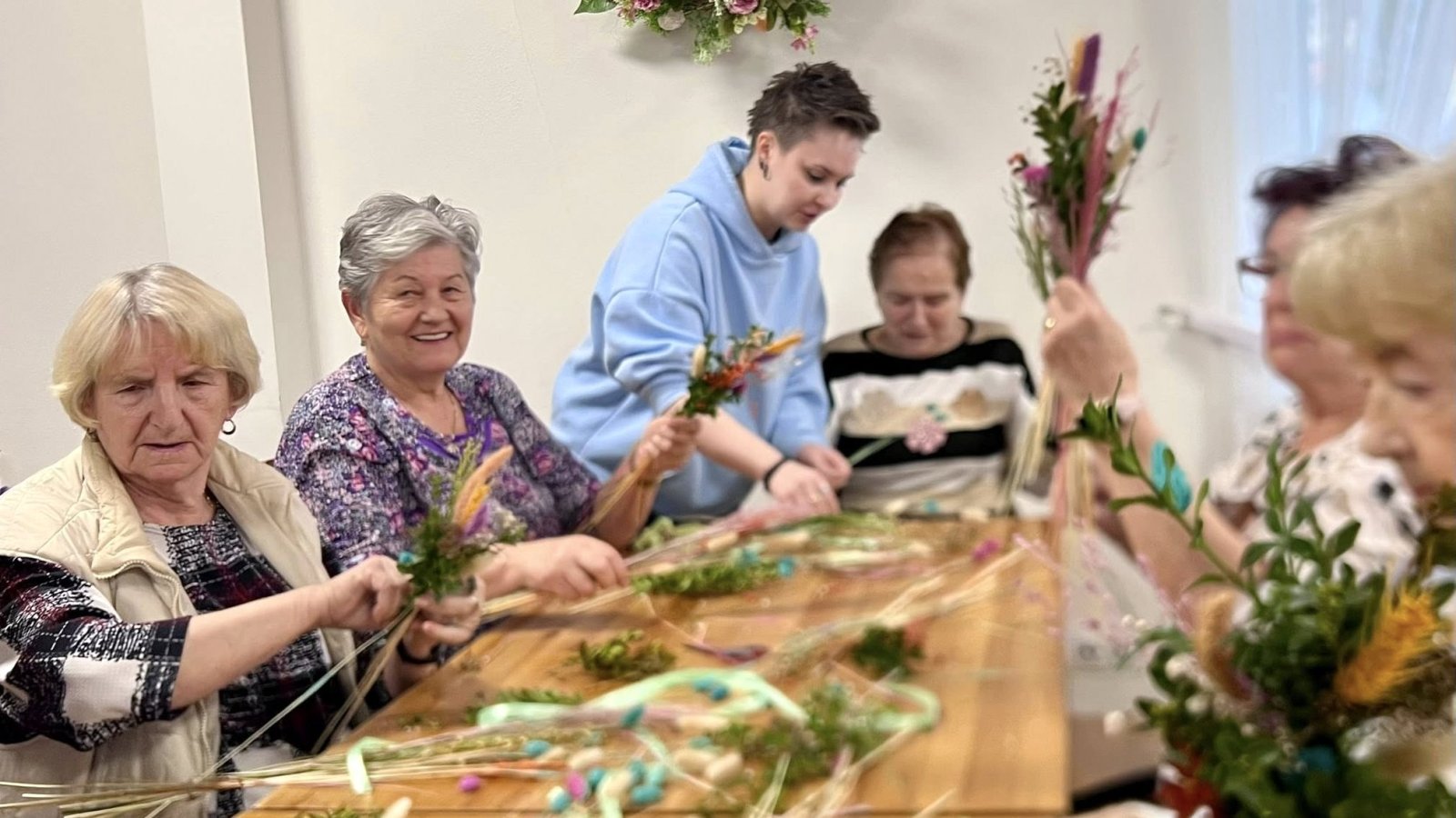 Seniorki siedzące przy stole i przygotowujące bukiety z suszonych kwiatów
