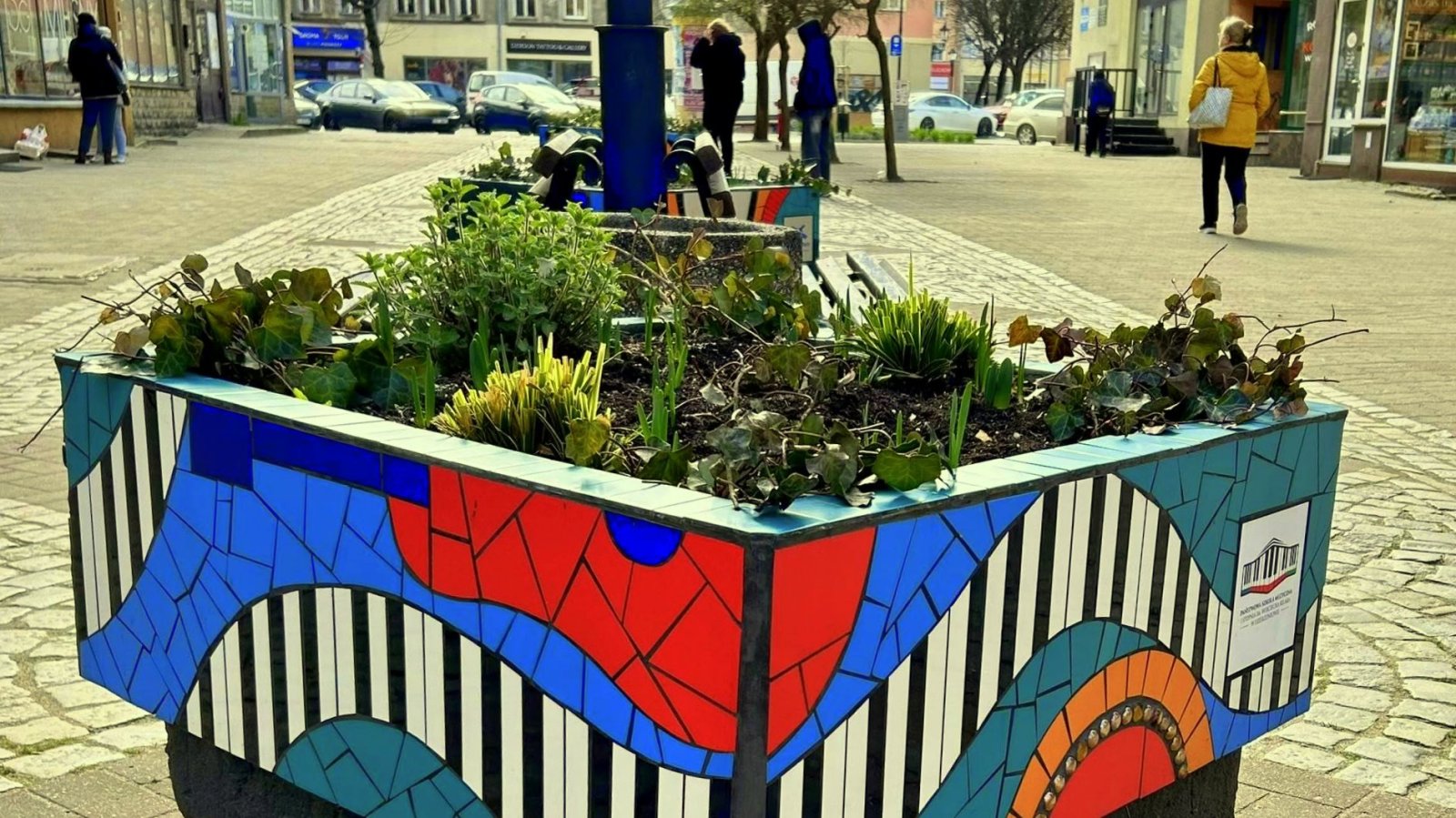 Deptak pieszy, na pierwszym planie duża donica z ceramiczną mozaiką