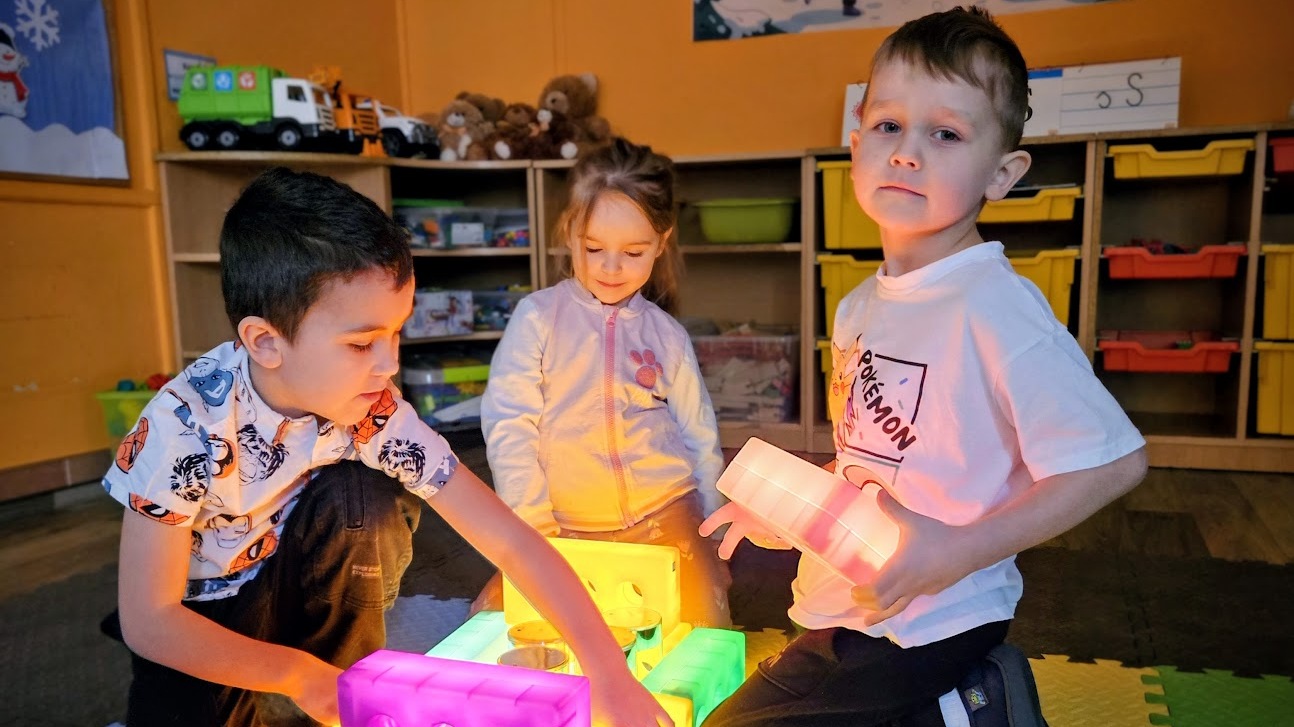 Dwóch chłopców i dziewczynka bawiących się świecącymi klockami