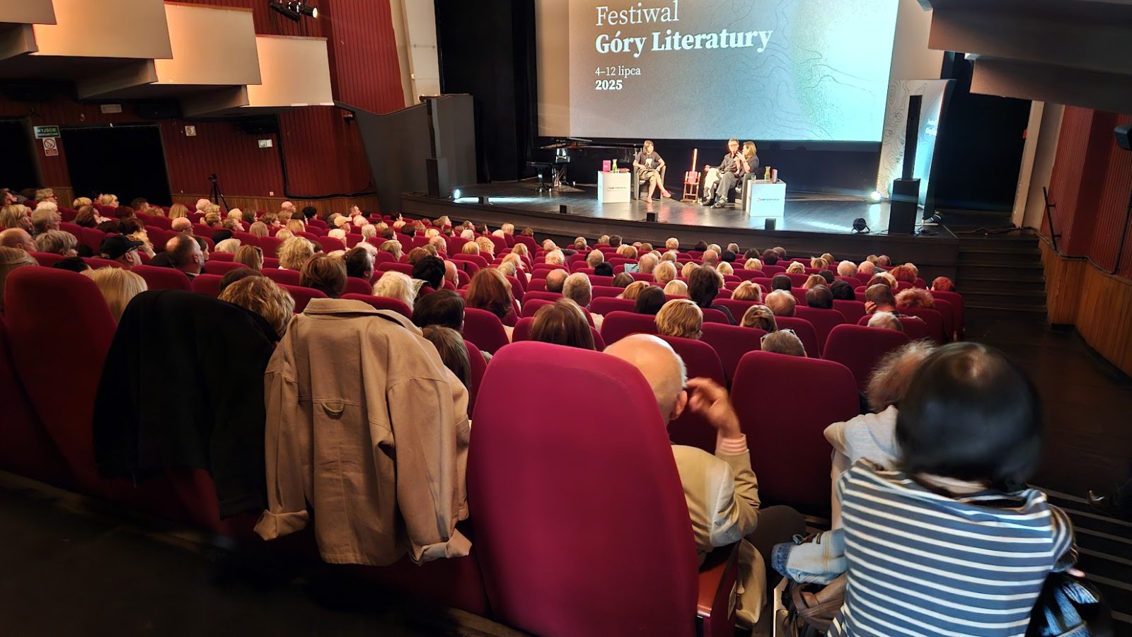 Kinoteatr, wypełniona sala, na scenie dyskusja trzech osób, na ekranie duży napis Góry Literatury