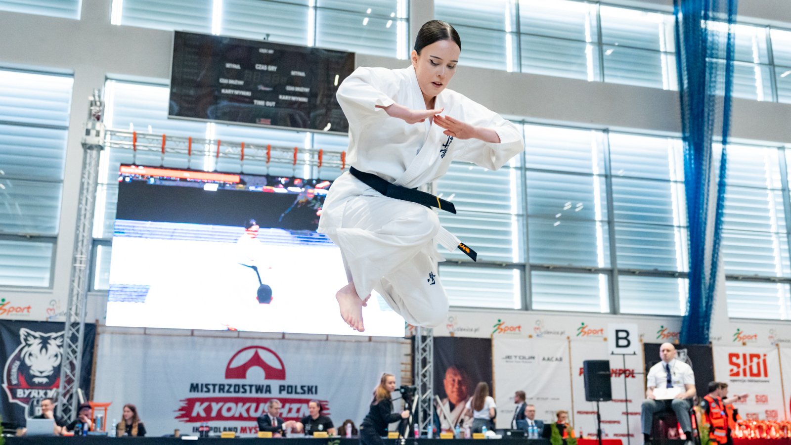 Dziewczyna w białeym stroju z czarnym pasie w wyskoku