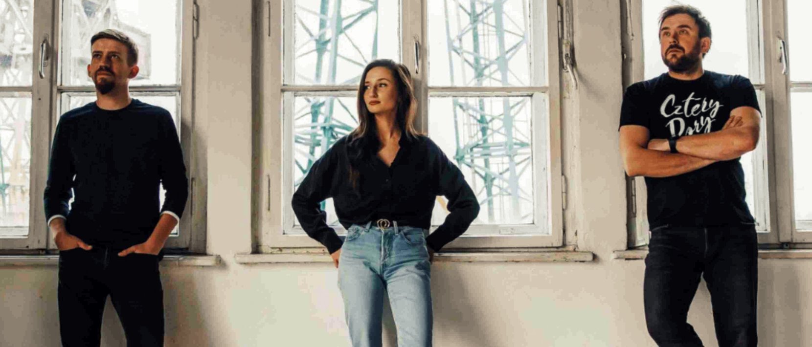 Członkowie zespołu - kobieta i dwóch mężczyzn stojących przy oknach