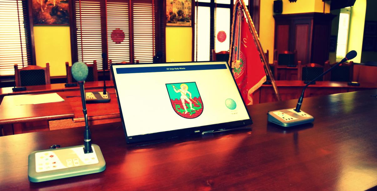 Widok stołu prezydialnego rady z monitorem na którym jest herb Dzierżoniowa
