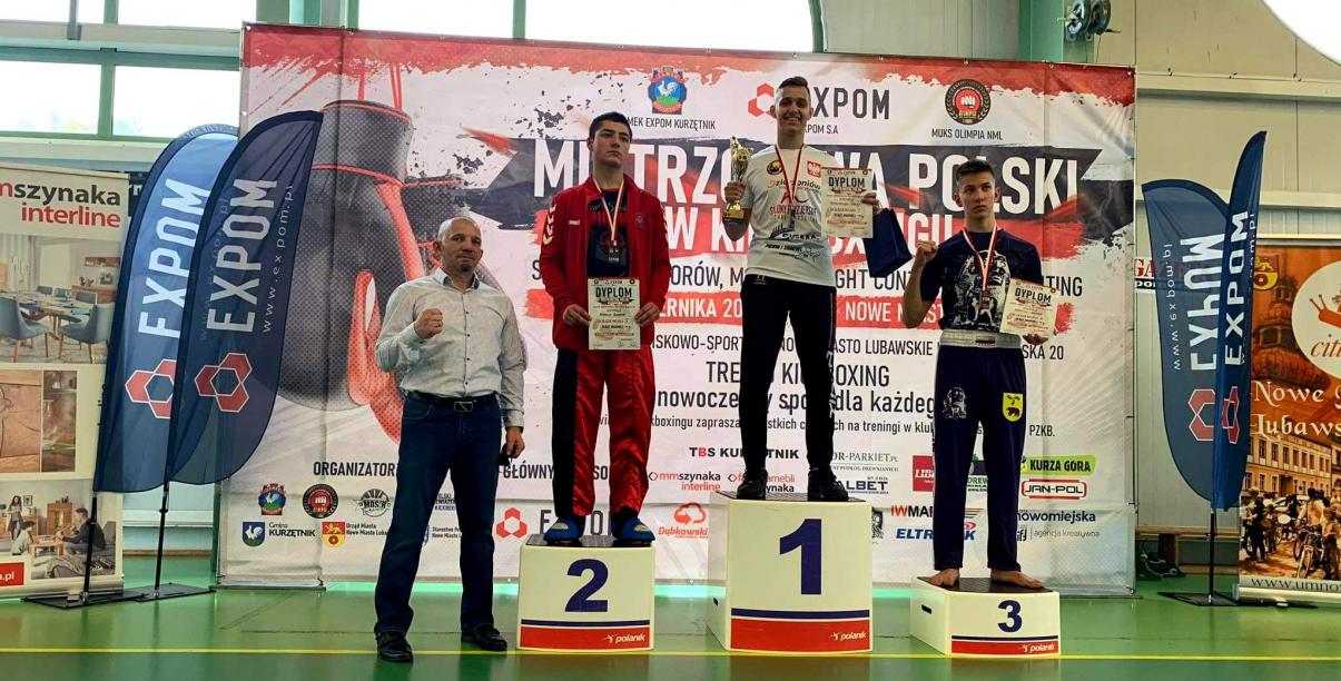 Maksymilian Palej na najwyższym stopniu podium, obok inni zawodnicy i trenerzy