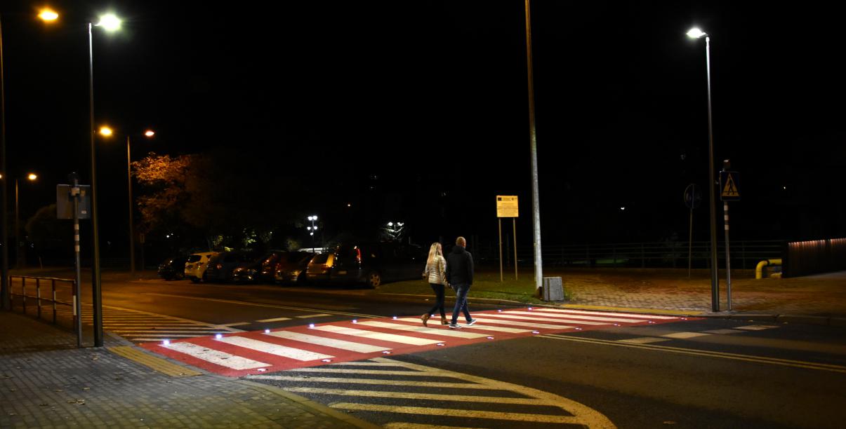 Dobrze oświetlone przejscie dla pieszych, przez które przechodzi para mieszkańców