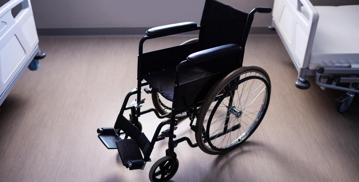 Na zdjęciu puste łóżka rehabilitacyjne i wózek inwalidzki 