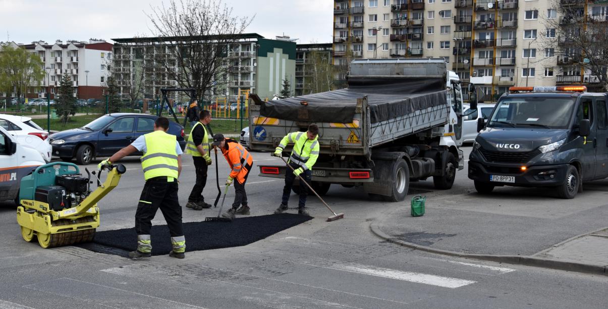 Czworo pracowników w żóltych kamizelkach łąta ubytek w drodze