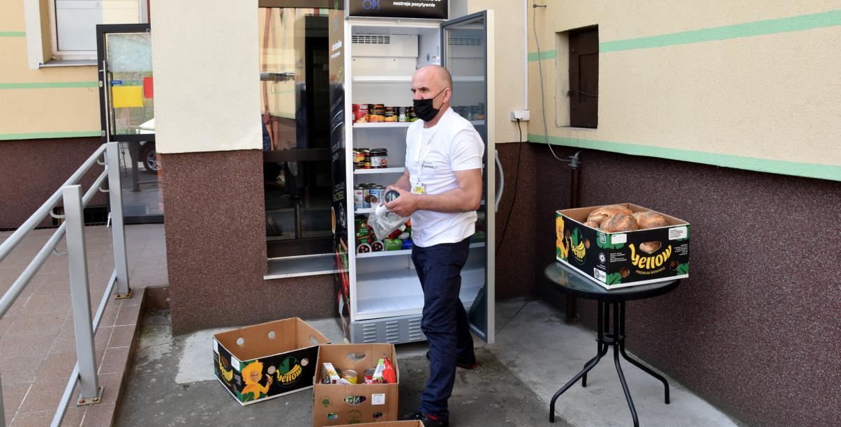 Mężczyzna wkładający jedzenie do lodówku przy wejściu do budynku OPS-u