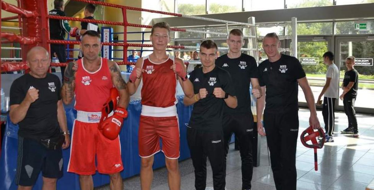 Grupa zawodników i trenerów stojąca rzed ringiem bokserskim 