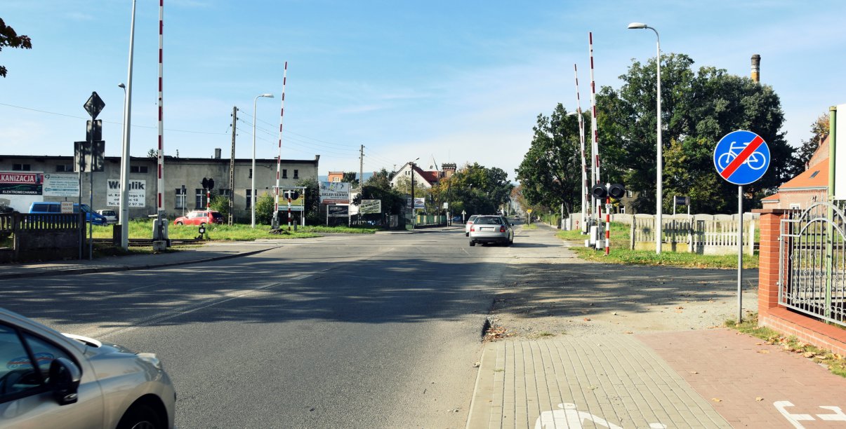 Przejad kolejowy, podniesione szlabany, w drugim planie droga