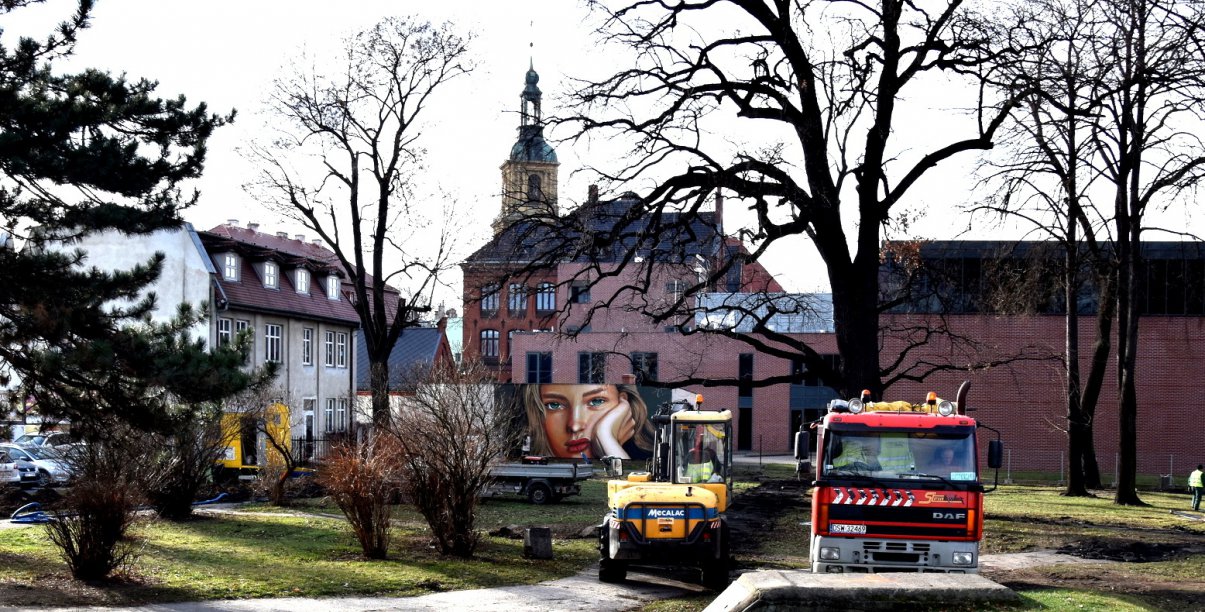 Park późną jesienią, pracująca koparka i stojący obok smochód ciężarowy