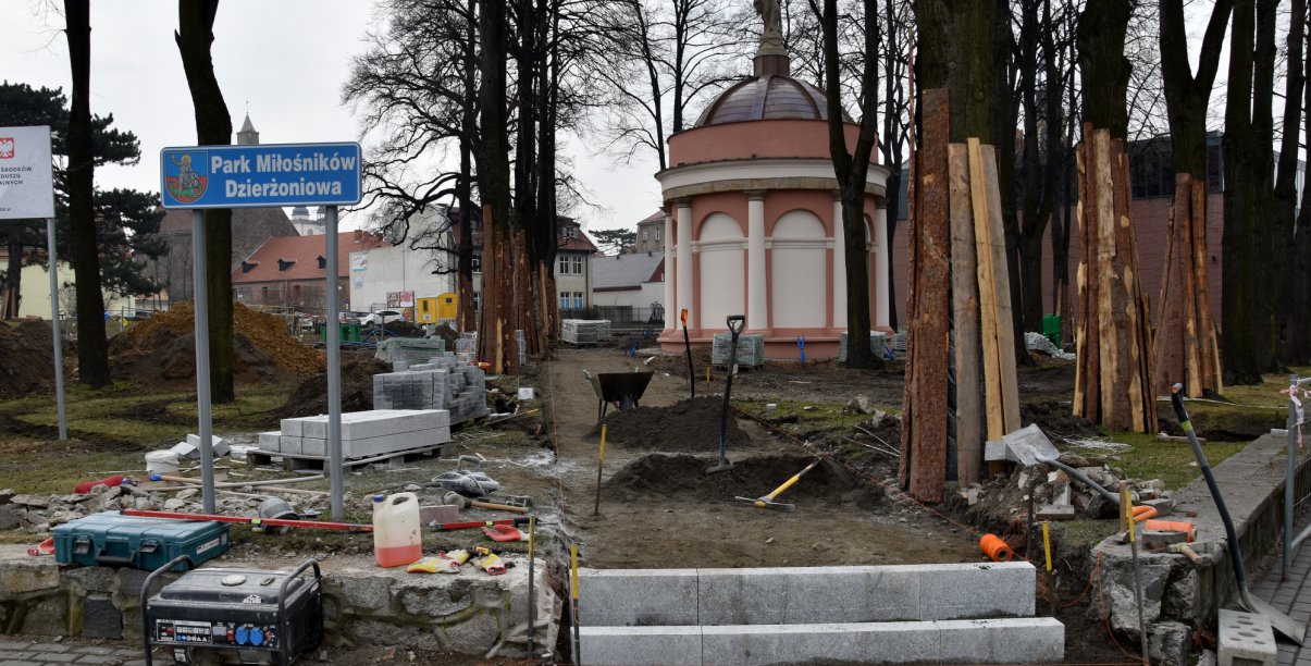 Park, w trackie remontu, drzewa zabezpieczone deskami i schody na pierwszym planie 