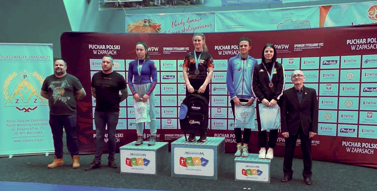 Spotrowcy na podium, obok podium stojący trenerzy