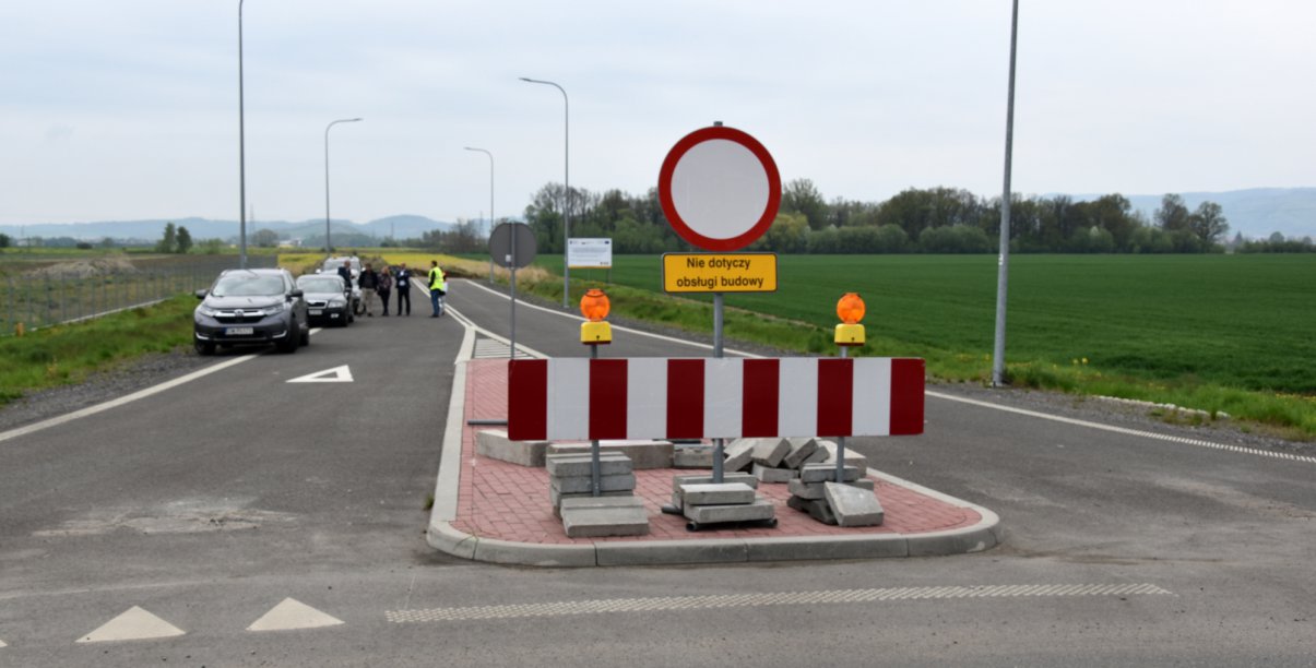 Droga ze znakiem zakazu wjadu zagrodzona barierką, w drugim planie grupka ludzi