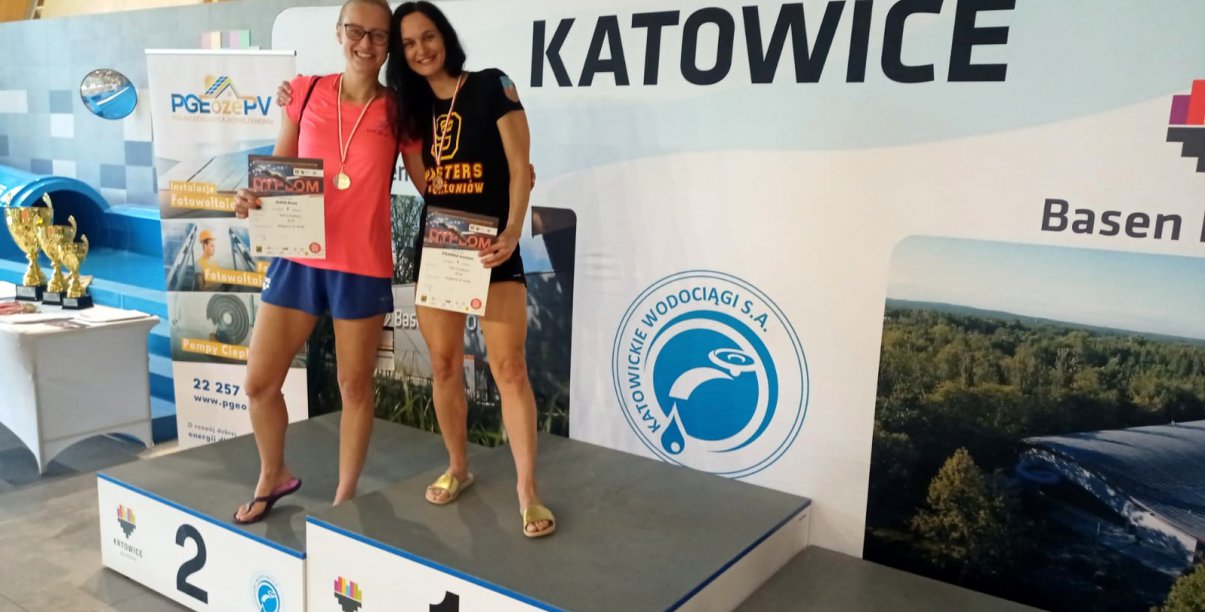 Dwie uśmiechnięte zawodniczki na podium, obok napis Katowice
