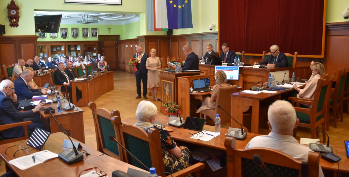 Sesja rady miejskiej, sala pełna osób siedzących rpzy stołach