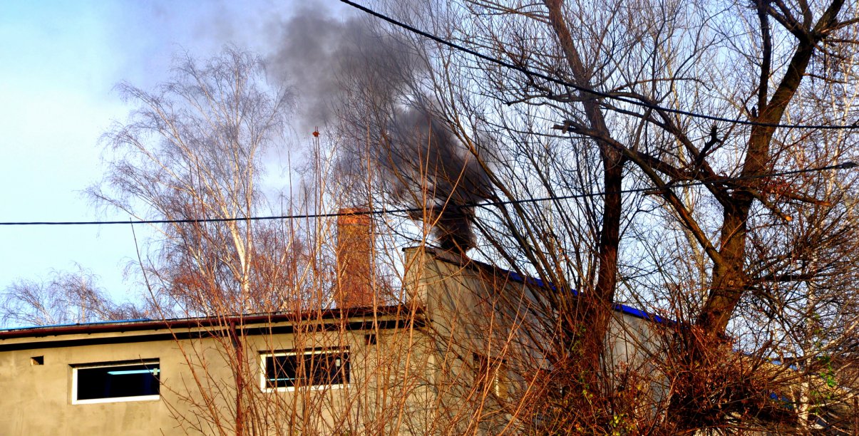 Dach budynku i czarny dym wydobywający się z komina