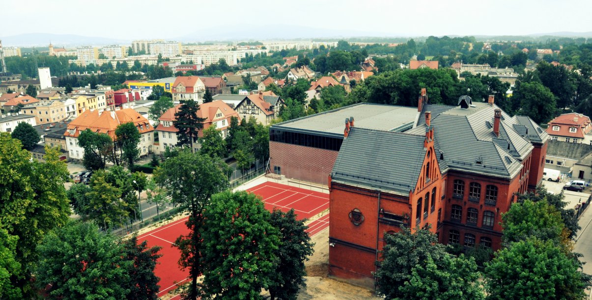 Fragment miasta z góry, na pierwszym planie duży budynek z cegły i boisko 