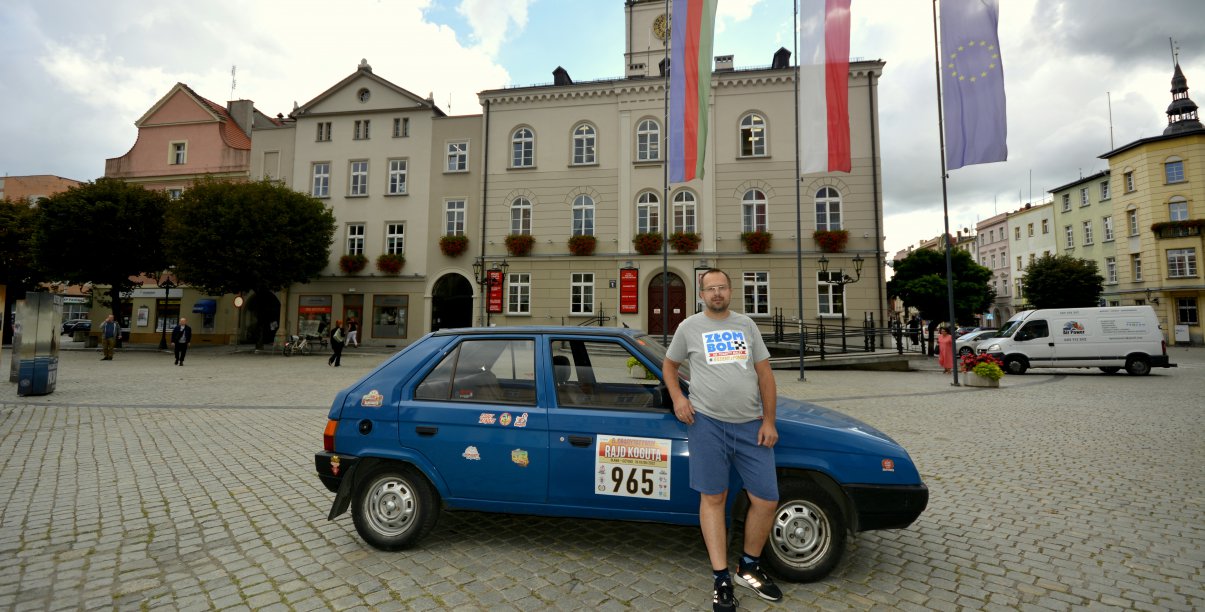 Mężczyzna stojący przy samochodzie, w drugim planie ratusz