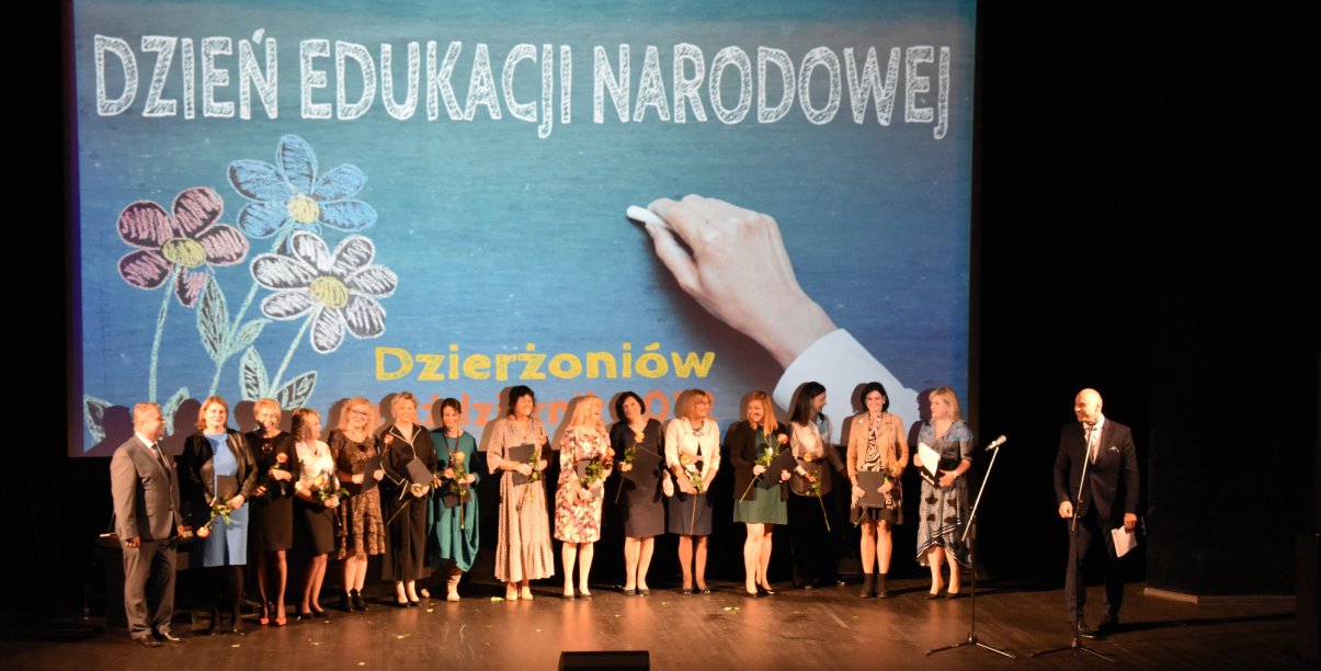 Grupowe zdjęcie nauczycielek na scenie, z tyłu grafika z napisem Dzień Edukacji